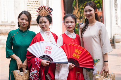 身穿古裝的中國游客和身穿越南傳統(tǒng)服飾奧黛的越南青年在文廟門前合影。